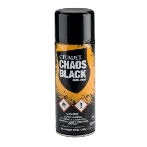 Photographie sur fond noir uni de la bombe aérosol de sous-couche Chaos Black de la gamme Citadel. La canette métallique noire est surmontée d'un grand capuchon cylindrique en plastique noir opaque. L'habillage graphique central met en scène une éclaboussure orange et jaune vif qui détache un blason noir. À l'intérieur de ce blason, le nom de la marque "CITADEL" et le nom du produit "CHAOS BLACK" sont inscrits en lettres capitales blanches, suivis de la mention "MODEL PAINT". Au bas de la bouteille, deux logos de sécurité en forme de losange blanc bordé de rouge signalent un produit inflammable et irritant, surmontant des blocs de texte réglementaires blancs indiquant notamment la contenance de "400ml" et un logo de restriction d'âge "16+".