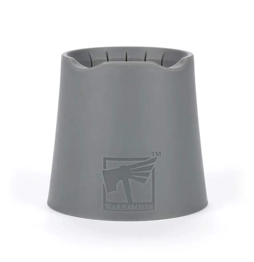 Photographie de studio sur fond blanc présentant un pot à eau warhammer de la marque Citadel. L'objet est un récipient en plastique gris mat, de forme tronconique évasée vers le bas pour une stabilité maximale. Le logo officiel Warhammer avec l'icône de la comète à deux queues est gravé en relief sur la face avant. Le bord supérieur présente des encoches arrondies pour poser les pinceaux, et l'intérieur laisse deviner des stries verticales conçues pour frotter les poils des pinceaux et éliminer les résidus de peinture efficacement.