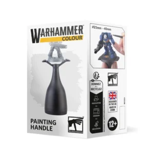Emballage en carton blanc vu de trois-quarts présentant la poignée de peinture Warhammer Colour. La face avant affiche le logo officiel noir et jaune au-dessus d'une illustration centrale montrant le manche ergonomique noir qui maintient fermement les jambes d'une figurine en plastique gris en cours d'assemblage. En bas, figurent l'inscription "PAINTING HANDLE" et le logo carré du marteau ailé de Warhammer. La face latérale droite détaille la compatibilité pour des socles de 25 mm à 40 mm, illustrée par une photo en gros plan d'une main appliquant de la peinture au pinceau sur l'épaulette blanche d'un Space Marine bleu positionné sur l'outil. Des logos de recyclage et la mention d'âge "12+" complètent le côté de la boîte.
