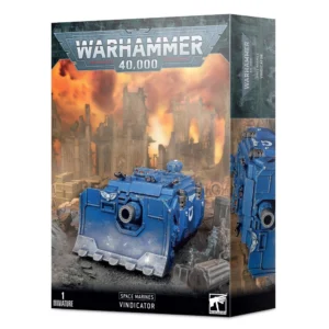 Boîte d'emballage officielle de la figurine Warhammer 40,000 présentant le char d'assaut des Space Marines. L'illustration principale met en scène le Vindicator, un imposant véhicule blindé chenillé peint en bleu, la couleur emblématique du chapitre des Ultramarines. Ce char de siège est équipé à l'avant d'une gigantesque lame de bulldozer renforcée, ornée d'un symbole de crâne ailé blanc, d'où émerge un énorme canon central court et massif. Le flanc du véhicule arbore l'icône blanche du chapitre en forme de U. Le blindé progresse sur un terrain jonché de débris métalliques et de gravats gris. À l'arrière-plan, un paysage urbain dévasté révèle des ruines de cathédrales gothiques silhouettées contre un ciel de guerre embrasé par d'épaisses fumées et des lueurs orange et jaune. Le grand logo argenté Warhammer 40,000 domine le haut, tandis que les mentions textuelles "Space Marines" et "Vindicator" apparaissent en blanc sur la bande noire inférieure. Le côté droit de la boîte montre un visuel secondaire du char de profil.
