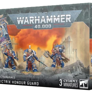 Vue en perspective de la boîte de jeu Warhammer 40,000 illustrant la Garde d'Honneur Victrix. Au centre, trois figurines de Space Marines Ultramarines en armure bleue et dorée, dont l'une brandit une grande bannière ornementée, sont posées sur un sol rocheux devant un paysage de ruines embrasé par un ciel orange vif. Le logo argenté "WARHAMMER 40,000" domine le sommet de la boîte. Le bandeau noir inférieur affiche les mentions "ULTRAMARINES", "VICTRIX HONOUR GUARD" et "3 CITADEL MINIATURES", avec le logo Warhammer blanc dans le coin inférieur droit. La tranche supérieure droite répète le nom de la faction et du produit sous le symbole de l'épée ailée.