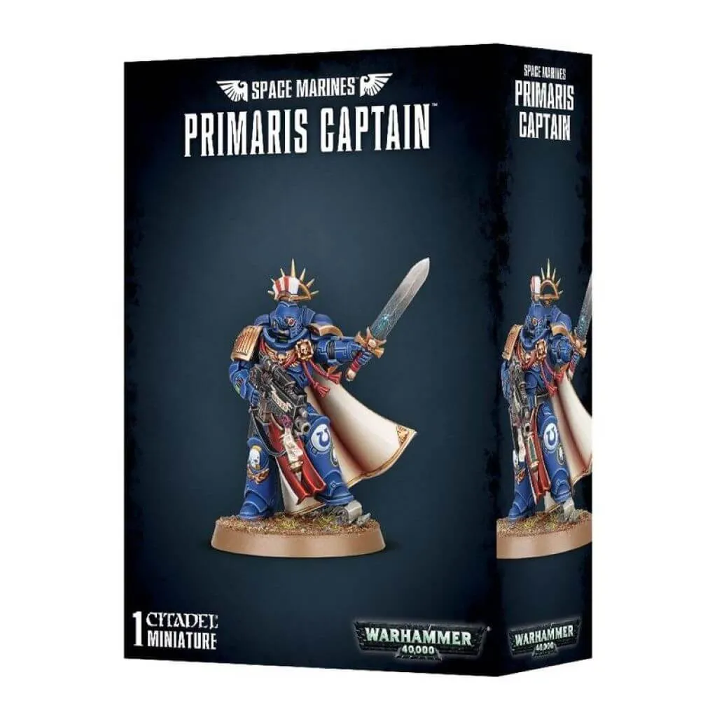 Vue de trois quarts de la boîte de figurine officielle pour le jeu Warhammer 40,000. L'emballage arbore un design moderne gris foncé et noir texturé. En haut au centre, les inscriptions blanches en lettres capitales indiquent « SPACE MARINES PRIMARIS CAPTAIN » sous un logo d'ailes impériales. L'illustration centrale met en scène la figurine peinte d'un Space Marine Captain debout sur un socle de terre et d'herbe, se détachant sur un fond dégradé bleu nuit. Le guerrier est revêtu de l'armure assistée bleu saphir des Ultramarines avec des ornements dorés, une longue cape blanche et une auréole de fer dorée surmontant un cimier à plumes rouge et blanc. De sa main droite, il tient un fusil bolter lourd équipé d'une lunette, et brandit une épée énergétique de sa main gauche levée. Au bas de la boîte, on retrouve la mention blanche « 1 CITADEL MINIATURES » à gauche et le logo officiel métallique « WARHAMMER 40,000 » à droite.