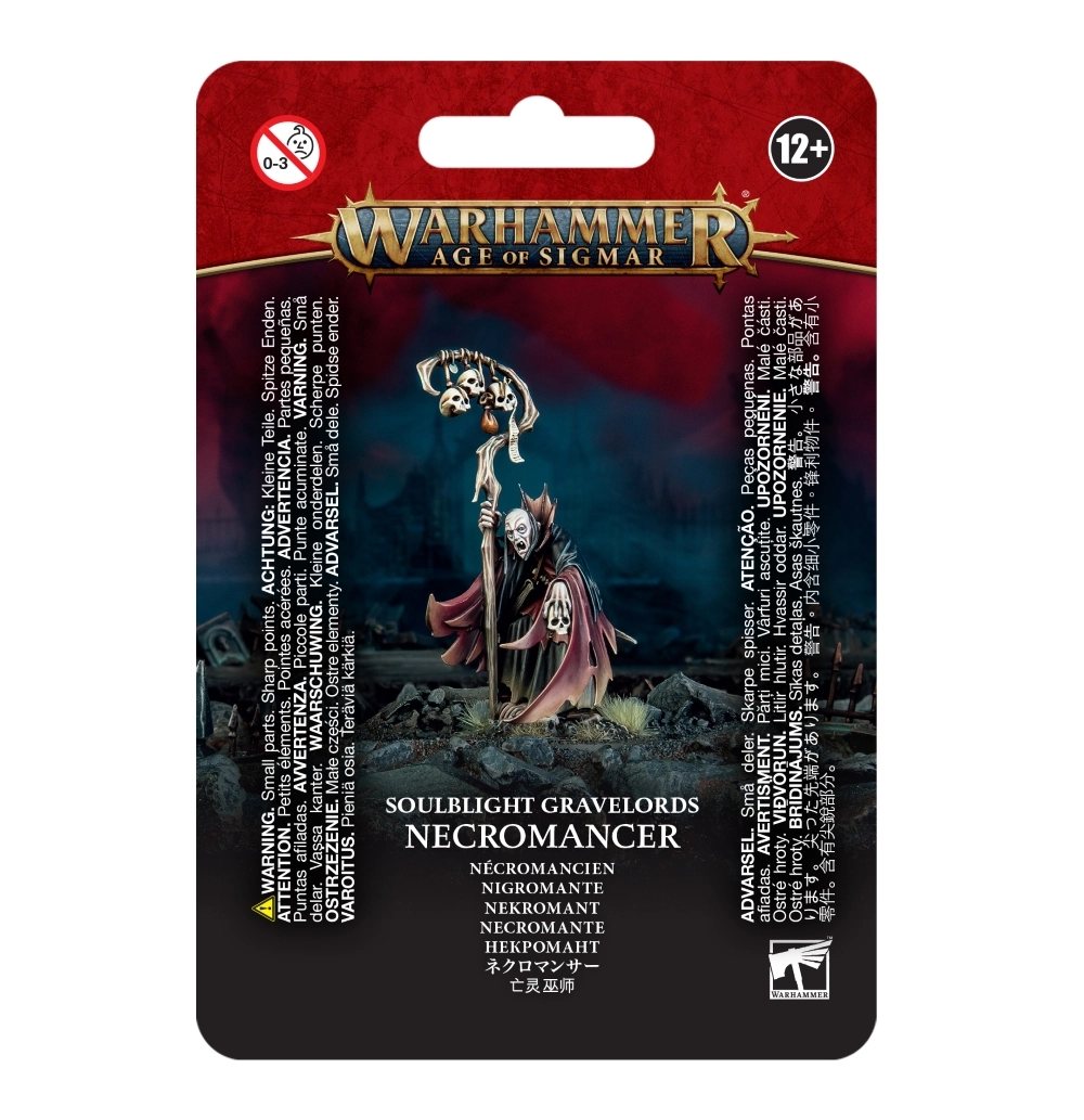 Emballage sous blister d'une figurine pour Warhammer Age of Sigmar avec un bandeau rouge supérieur portant le logo officiel doré. Au centre, la figurine peinte d'un Nécromancien des Soulblight Gravelords se dresse sur un sol rocheux et sombre. Ce sorcier blême aux yeux caverneux porte une robe déchirée sombre doublée de rouge ténébreux. Il tient dans sa main droite un grand bâton en bois surmonté de trois crânes et d'un parchemin, et tient un crâne humain dans sa main gauche. En dessous, le texte indique la faction « SOULBLIGHT GRAVELORDS » ainsi que le nom de l'unité « NECROMANCER / NÉCROMANCIEN ».