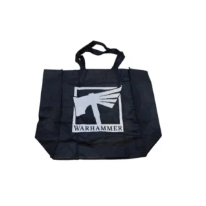 Un sac en tissu noir de type Tote Bag Warhammer est photographié de face, posé à plat sur un fond blanc uni. Au centre du sac, un grand imprimé blanc met en valeur le logo classique de la marque : un marteau de guerre stylisé avec une aile de plume s'étendant sur la droite, le tout entouré d'un cadre carré. Juste en dessous, le mot « WARHAMMER » est inscrit en lettres capitales blanches très nettes. Deux anses en tissu noir assorti sont fixées sur le bord supérieur du sac, qui présente de légers plis naturels sur sa surface textile.